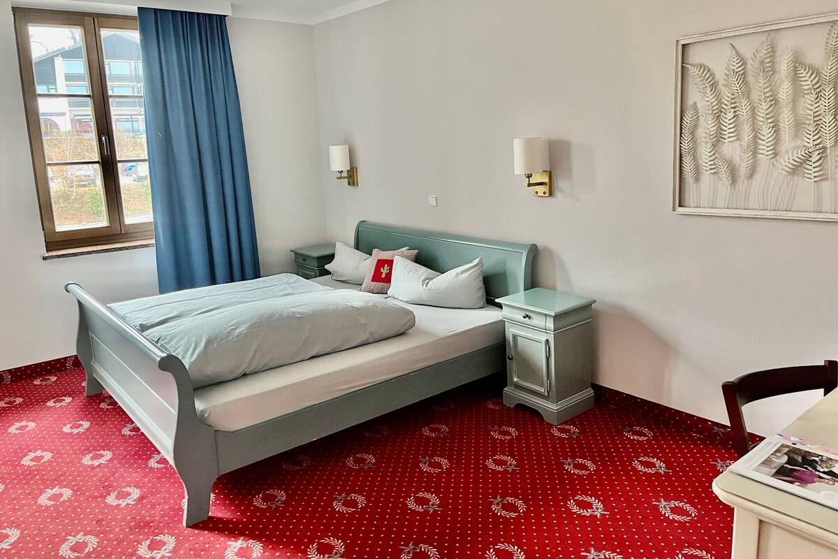 A hotel room with a bed, a nightstand, a lamp, a chair, and a window with curtains.