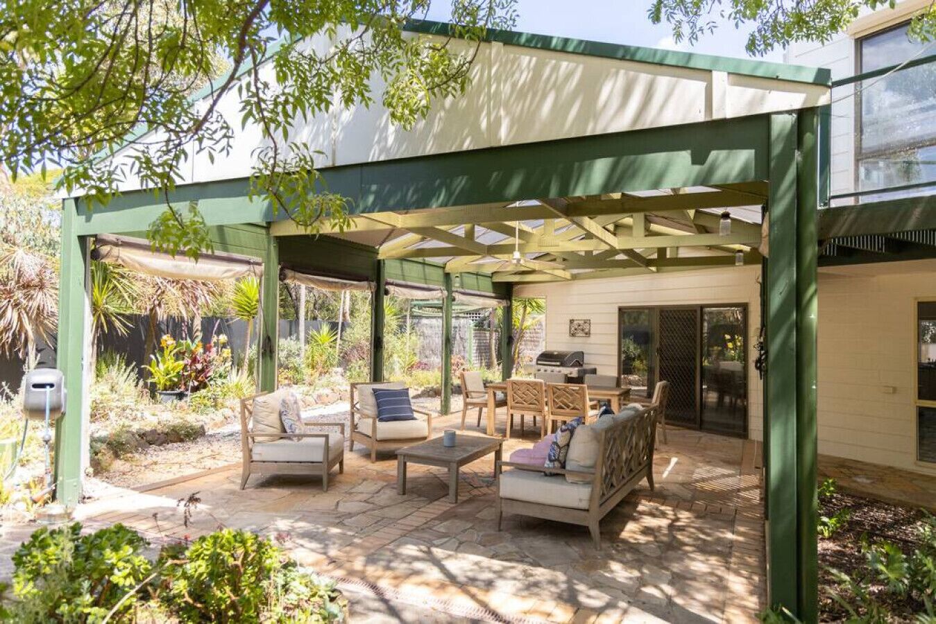 A covered patio with outdoor furniture, a grill, and a garden area.