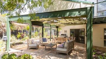 A covered patio with outdoor furniture, a grill, and a garden area.