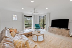 A modern living room with a leather sofa, a teal armchair, a round coffee table, a flat-screen TV, and large windows. - Sunnymead Heated Pool Retreat (Aireys Inlet)