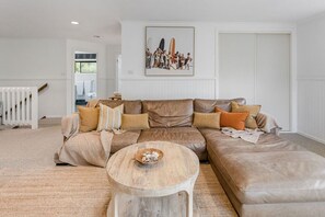 A living room with a large L-shaped sectional sofa, a round wooden coffee table, and a framed artwork above the sofa. - Sunnymead Heated Pool Retreat (Aireys Inlet)