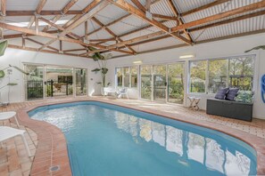 An indoor swimming pool with a brick border, large windows, and a wooden ceiling structure. - Sunnymead Heated Pool Retreat (Aireys Inlet)