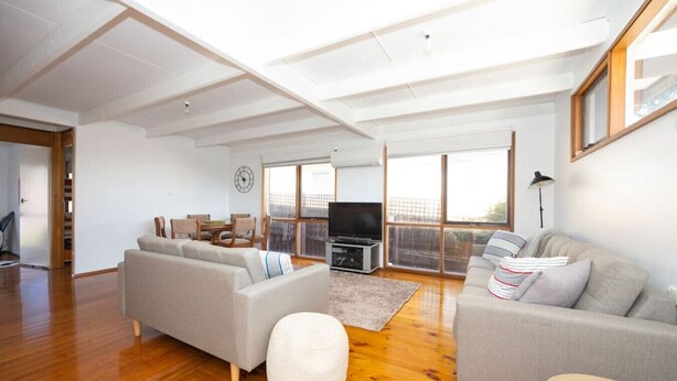 A spacious living room with a large sofa, a smaller sofa, a round ottoman, a TV, and a dining area with chairs and a table. - Bush Serenity  - Anglesea (Anglesea)