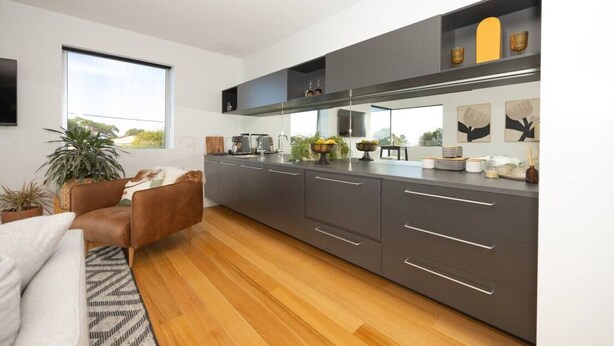A modern kitchen with grey cabinets, a wooden countertop, and a built-in oven. There is a dining area with a brown leather chair and a large window.