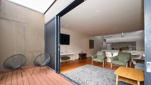 A modern living space with a wooden deck, two black wireframe chairs, a grey rug, and a small wooden table.