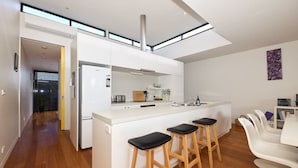 A modern kitchen with a central island, bar stools, and a dining area with white chairs.