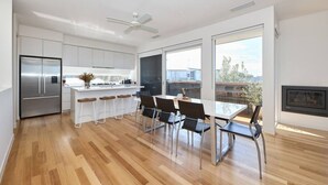 Una cocina moderna con un refrigerador de acero inoxidable, una barra con taburetes, una mesa de comedor con sillas y una chimenea.