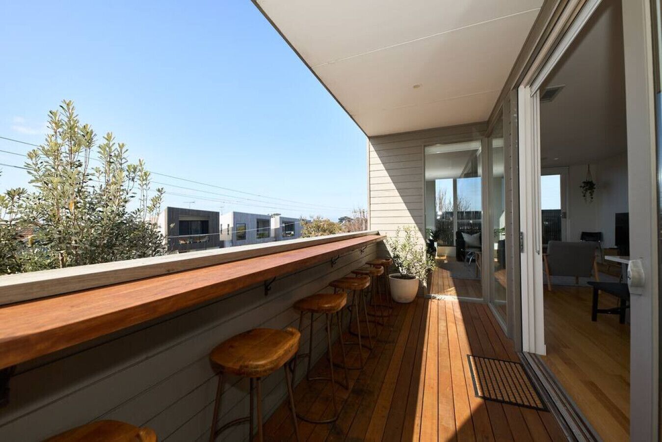 Un balcon moderne avec un plancher en bois, un comptoir de bar en bois et plusieurs tabourets.