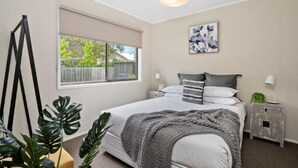 Un dormitorio con cama, mesitas de noche, ventana y lámpara en el techo.