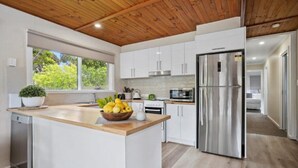 Una cocina moderna con armarios blancos, un refrigerador de acero inoxidable y techo de madera.