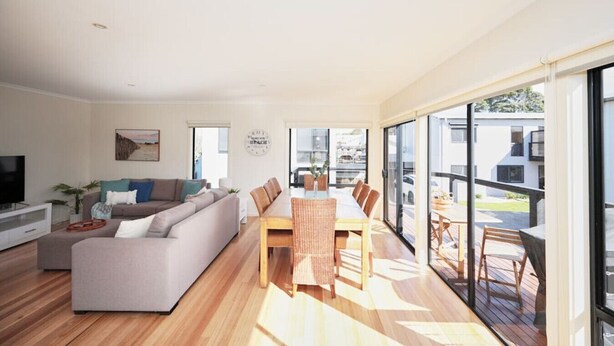 A modern living room with a sofa, dining table, and chairs. There is a TV, a plant, and a clock on the wall.