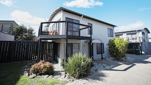 A modern two-story house with a balcony, a fenced yard, and a small garden.