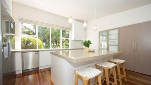 Cozinha moderna com uma ilha grande, banquetas de madeira e vista para o verde lá fora.