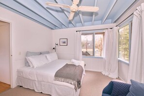 Une chambre à coucher avec un lit, un ventilateur de plafond, une fenêtre avec des rideaux et une porte.
