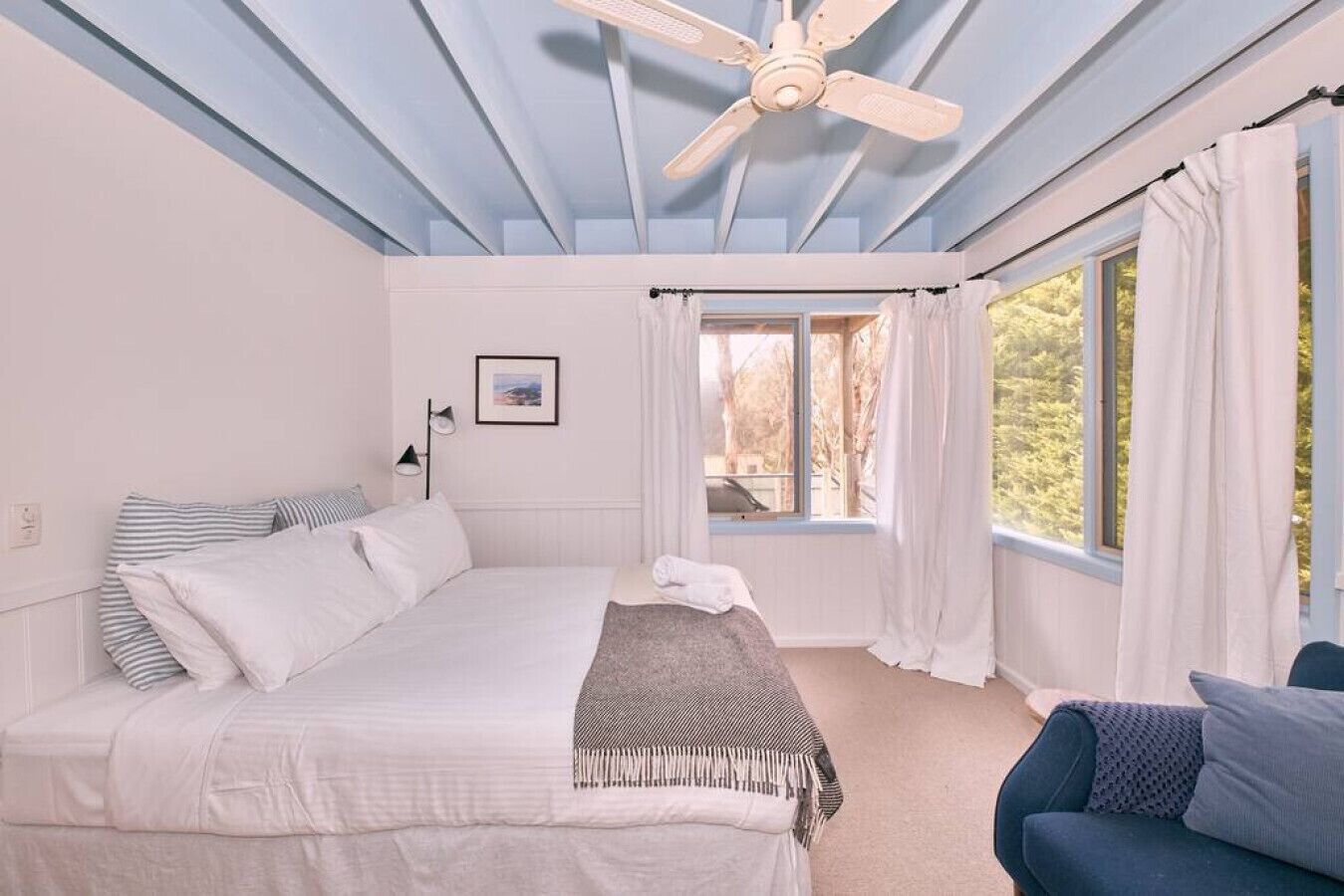 Une chambre à coucher avec un lit, un ventilateur de plafond, une fenêtre avec des rideaux et une vue sur les arbres à l’extérieur.