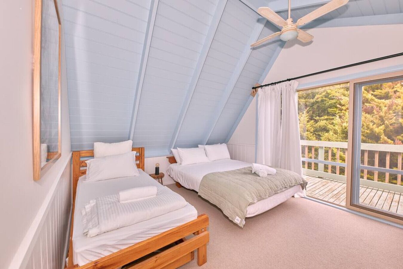 A bedroom with two beds, a ceiling fan, and a balcony with a view of trees.
