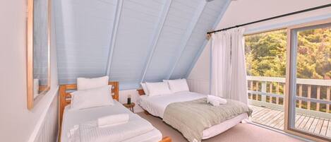 A bedroom with two beds, a ceiling fan, and a balcony with a view of trees.