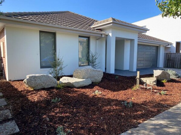 A modern single-story house with a white exterior, a tiled roof, and a front yard with mulch and rocks.