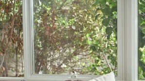 Un sofá seccional beige con almohadones a rayas y lisos, situado cerca de una ventana con vista a árboles.