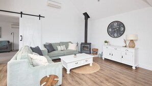 Una sala de estar con sofá, mesa de centro, mueble blanco, reloj y chimenea.