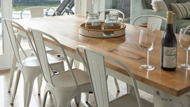 Un comedor con una mesa de madera, sillas blancas, una lámpara colgante de mimbre y vistas a un jardín trasero a través de amplios ventanales correderas.