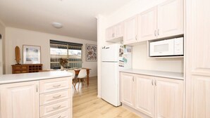 A modern kitchen with light wood cabinets, a white countertop, and a built-in microwave.