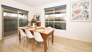 A dining area with a wooden table, white chairs, and a vase of flowers.