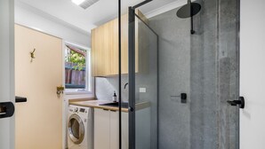 Ein kleines Badezimmer mit Waschmaschine, Duschkabine aus Glas und einem Fenster mit Blick auf Grünflächen.