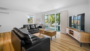 Ein modernes Wohnzimmer mit einem schwarzen Ledersofa, einem Holztisch und einem Fernseher auf einem Holzständer.