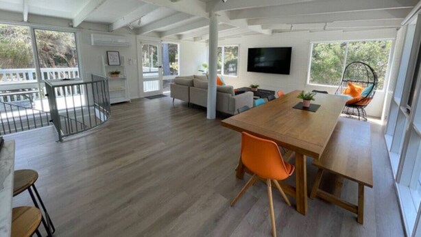 A spacious living area with a wooden dining table, orange chairs, a sofa, and a TV mounted on the wall. - Eagles Nest (Aireys Inlet)