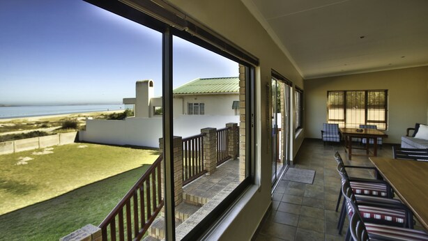 A balcony with a view of the beach, a dining area with chairs and a table, and a large window. - Oppi Stuppi Langebaan 4-Sleeper (Langebaan)