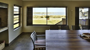 A dining area with a large table and chairs, a view of the beach, and a brick fireplace. - Oppi Stuppi Langebaan 4-Sleeper (Langebaan)