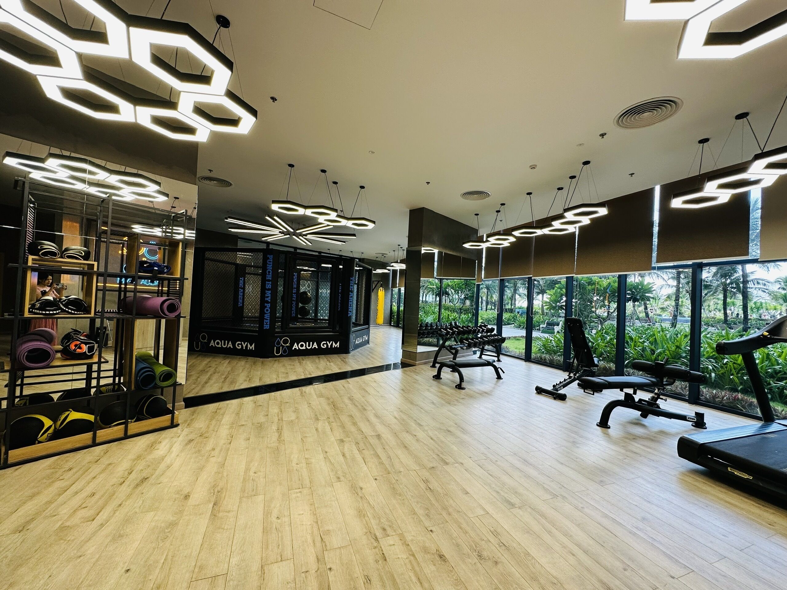 A gym with wooden flooring, exercise equipment, and a wall of yoga mats.