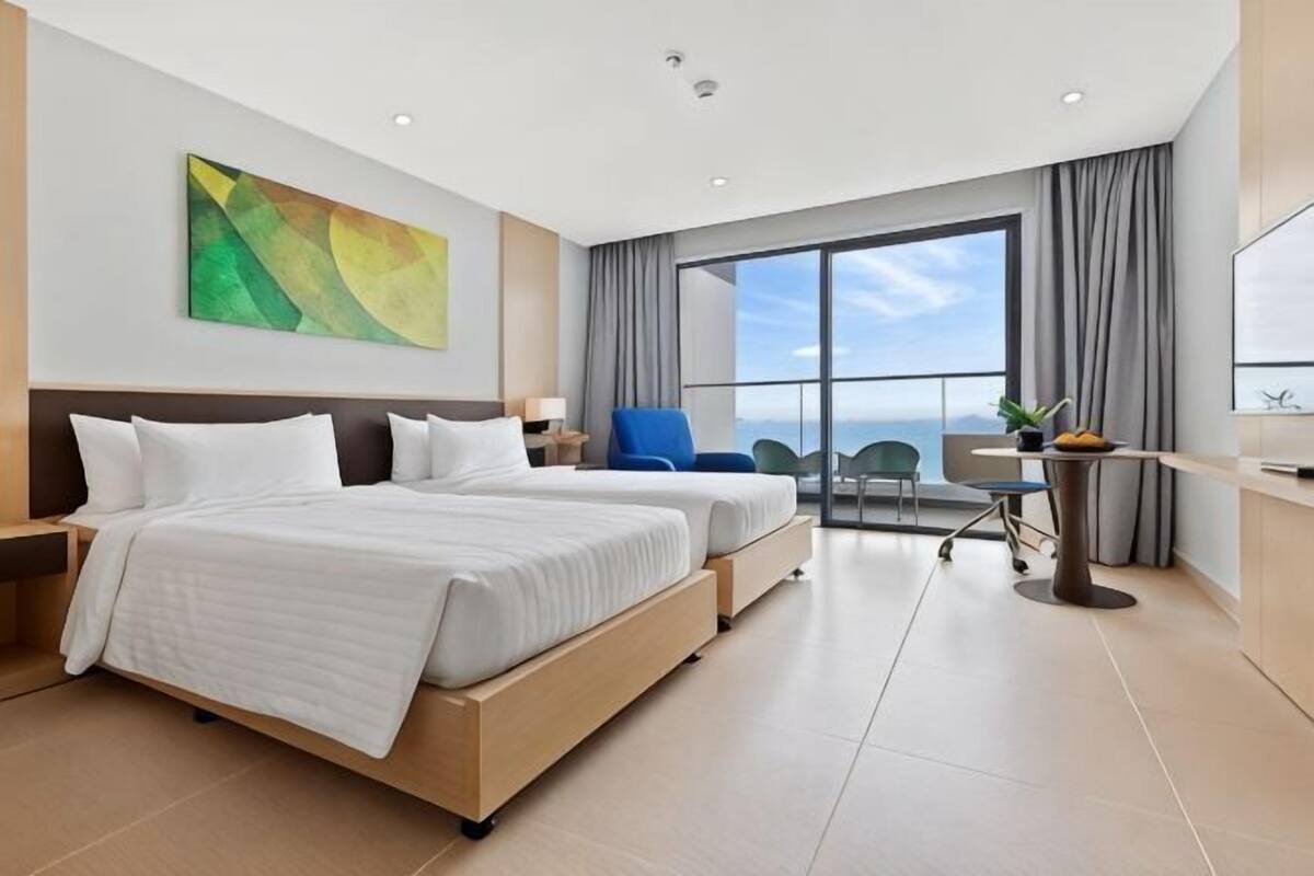 A hotel room with two beds, a large window with a view, a desk, and a chair.