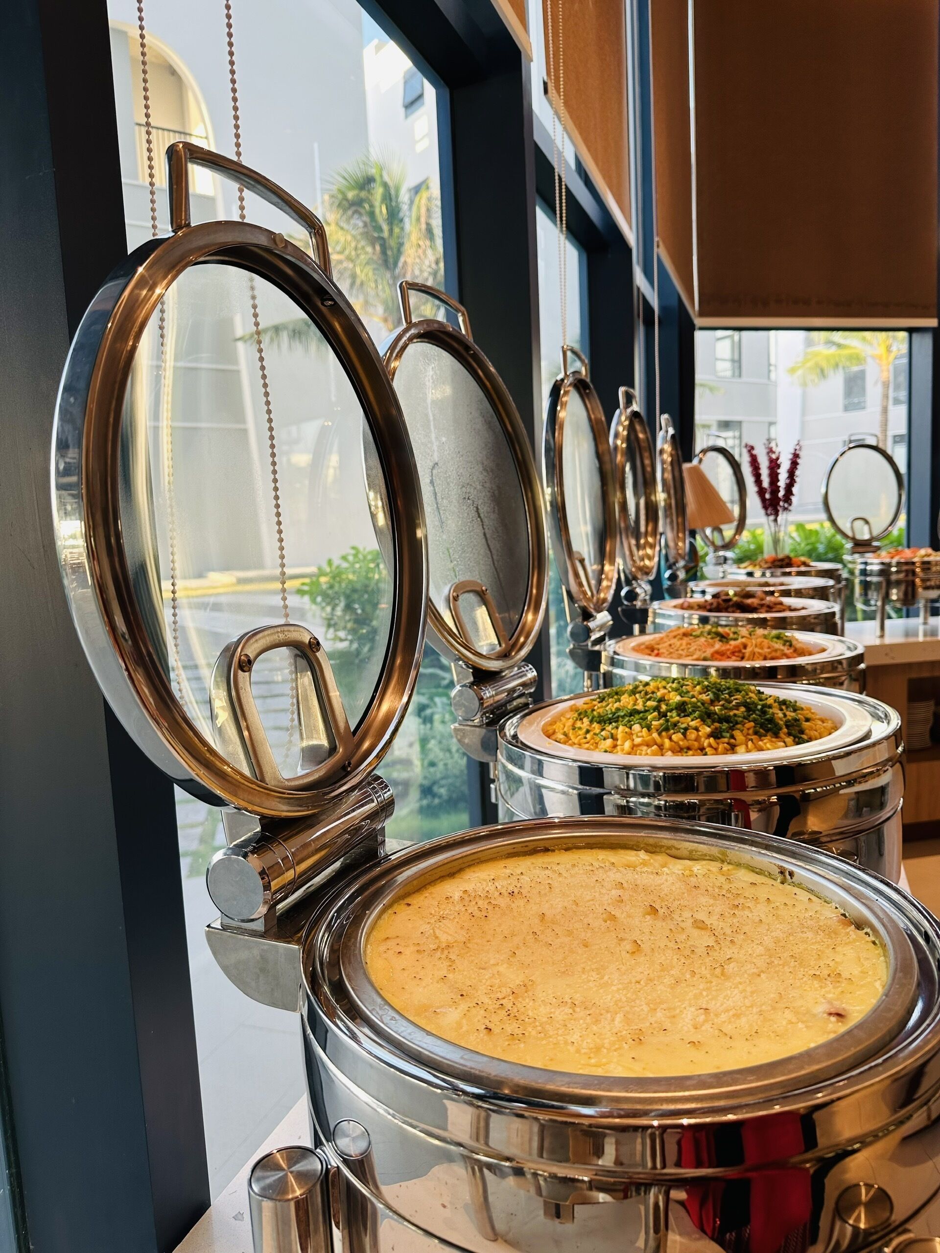 A buffet setup with multiple round stainless steel chafing dishes, some with lids open.