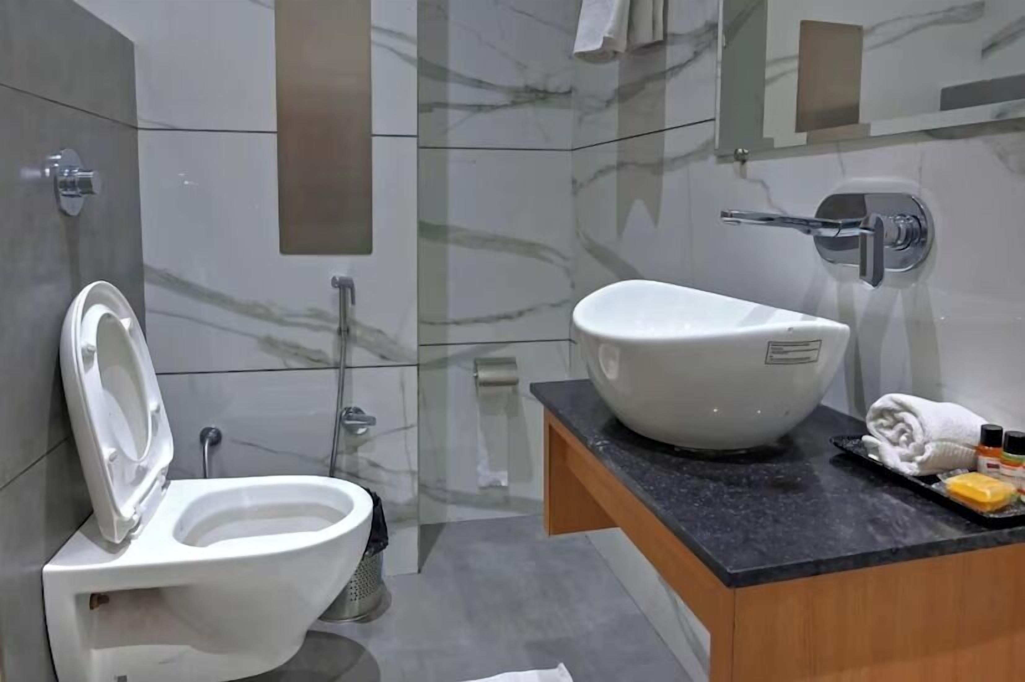 A modern bathroom with a white toilet, a large vessel sink, and a marble backsplash.