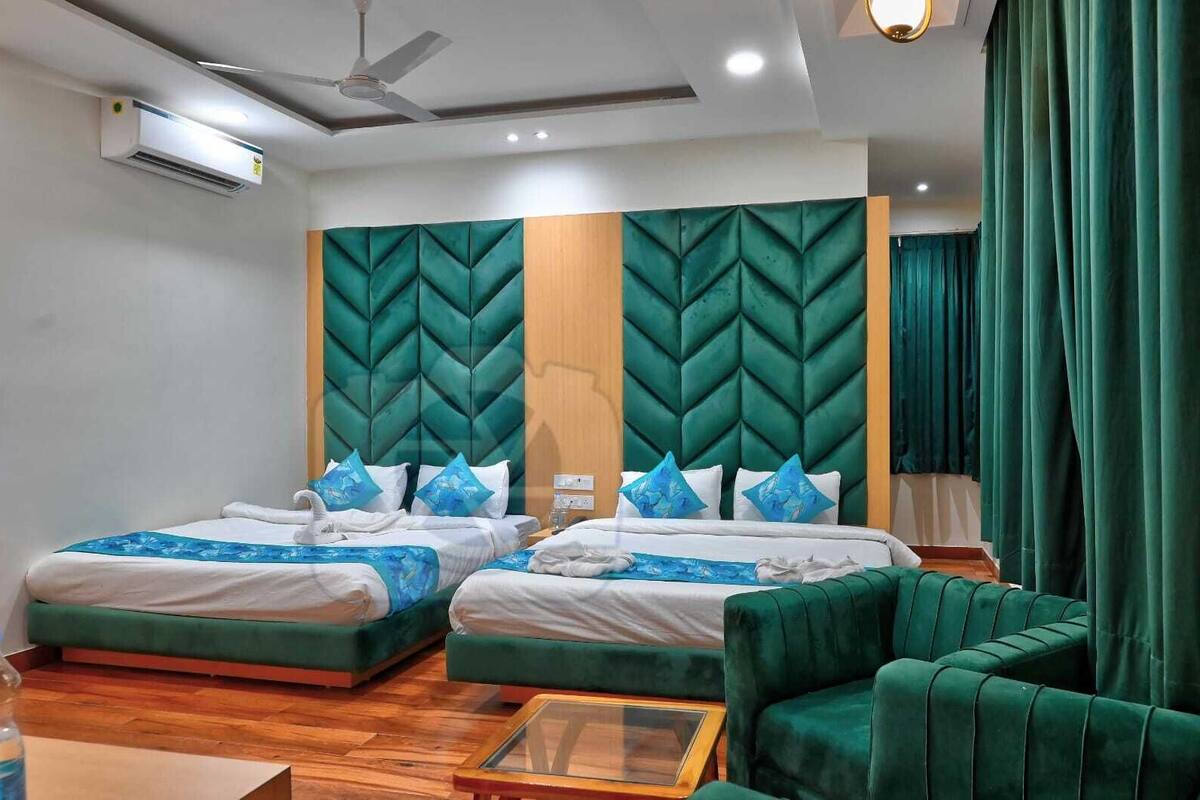 Ein Hotelzimmer mit zwei Betten, einem grünen Polstersofa, einem Holztisch und einem Deckenventilator.