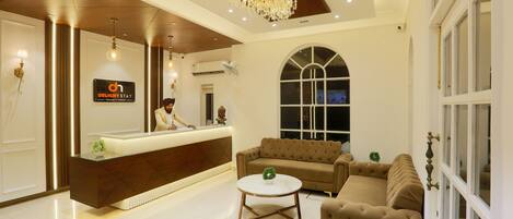 A hotel reception area with a reception desk, a chandelier, a sofa, and a large arched window.