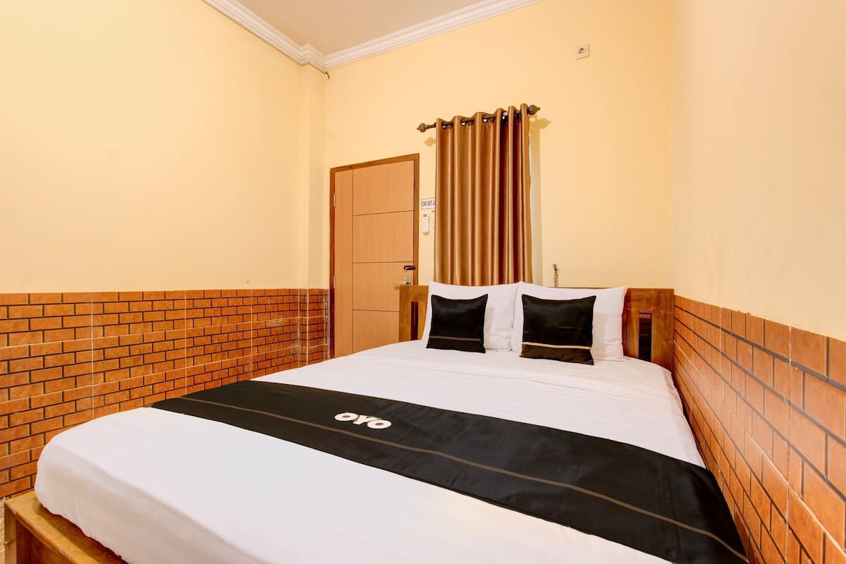 A hotel room with a brick-patterned wall, a wooden headboard, a bed with a black and white bedspread, and a curtain on the window.