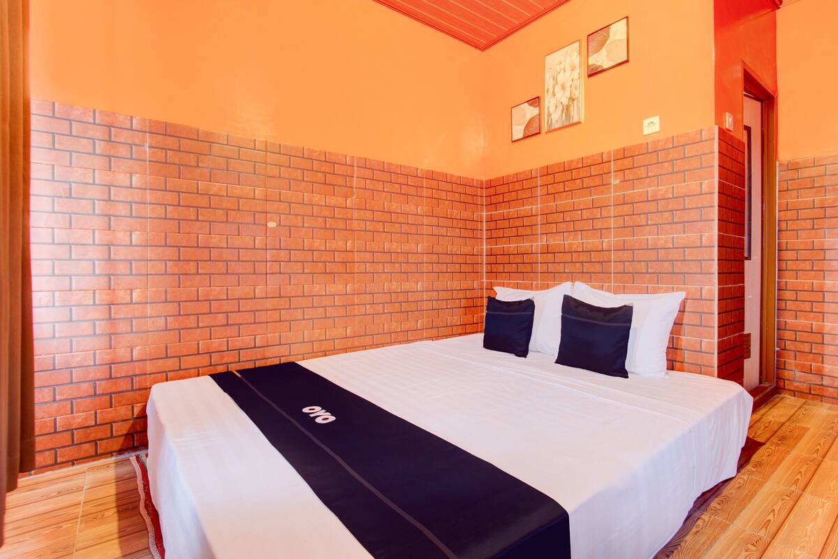 A hotel room with a brick-patterned wall, a bed with white and black bedding, and a wooden floor.