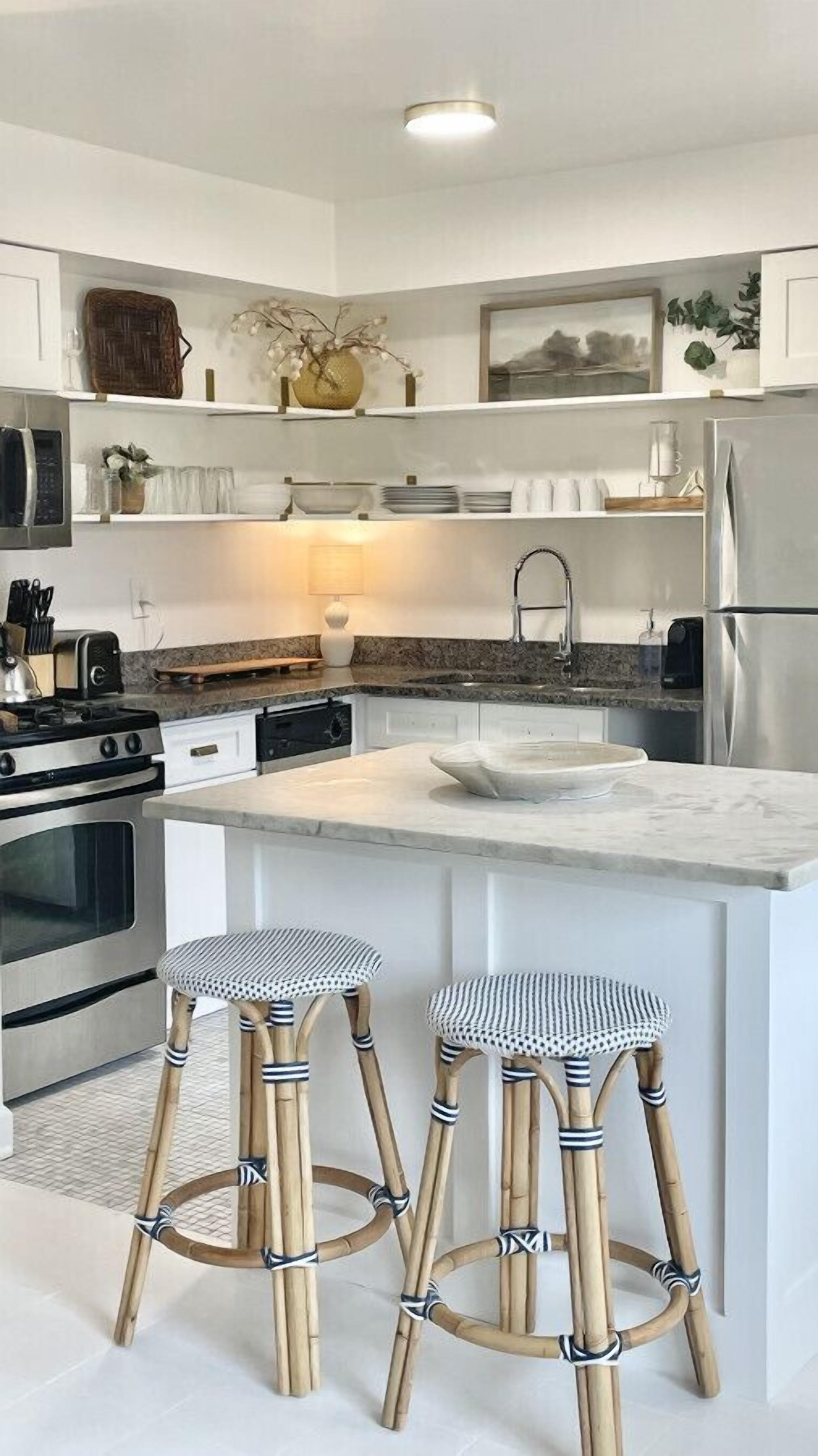 A modern kitchen with white cabinetry, a central island with a sink, two striped stools, and stainless steel appliances.