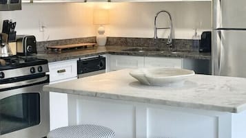 A modern kitchen with white cabinetry, a central island with a sink, two striped stools, and stainless steel appliances.