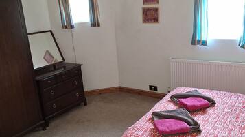 A bedroom with a bed, a dresser, a radiator, and two windows with curtains.