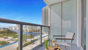 A balcony with a view of a cityscape, a chair, and a table with a bottle and a glass.