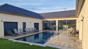 A modern outdoor pool area with a tiled deck, a small grassy area, and a seating arrangement with chairs and a table.