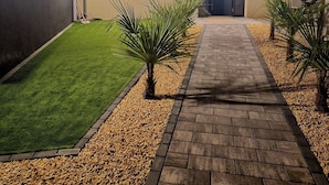A well-lit pathway leading to a house with a paved lawn and small palm trees.