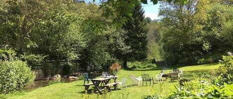 Um jardim exuberante com mesa e cadeiras para piquenique, cercado por vegetação densa e árvores.