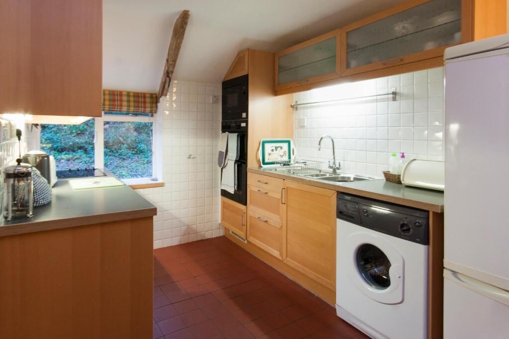 A compact kitchen with a washing machine, a sink, and a window with a view of greenery.