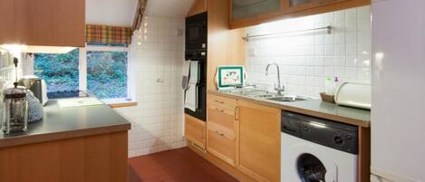 A compact kitchen with a washing machine, a sink, and a window with a view of greenery.