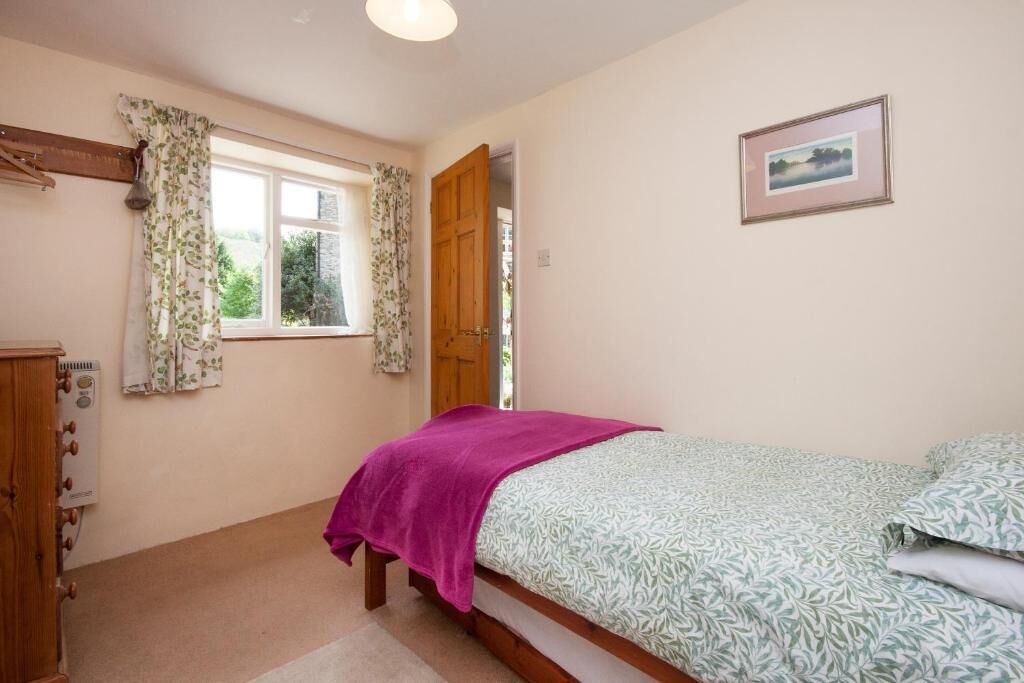 A bedroom with a bed, a window with curtains, a radiator, and a framed picture on the wall.